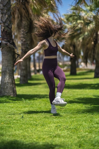 女人黑色背心和紫色紧身裤做瑜伽在绿色草地白天
